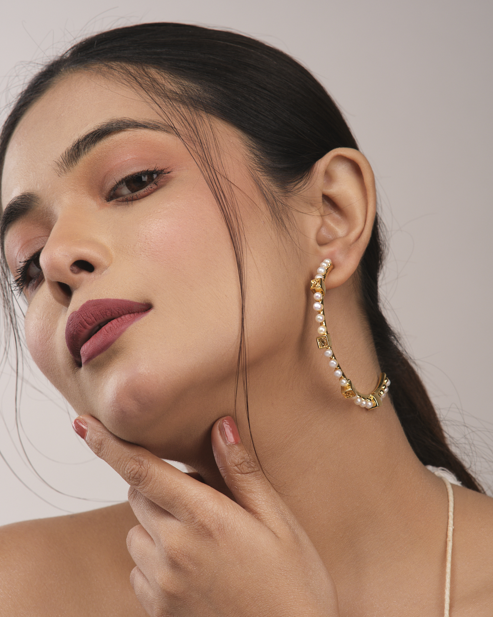 Close-up of a model wearing a pearl and gold hoop earring